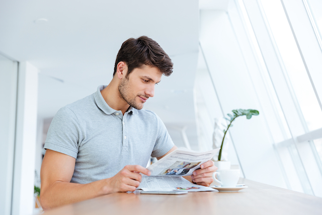 Confident young businessman reading newspaper and drinking coffee indoors